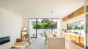 Una cocina moderna con una isla central, un área de comedor con sofá y un amplio ventanal con vistas a la vegetación.