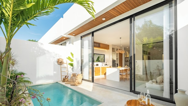 Una casa moderna con piscina, comedor y cocina visibles a través de amplios ventanales.