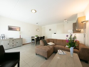 A modern living room with a brown sofa, a dining table, and a kitchen area in the background.