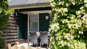 A wooden fence, a patio with two wicker chairs, and a building with a dark green exterior and a white door.