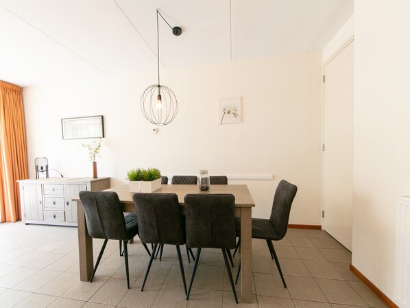 A dining area with a rectangular table, four chairs, a pendant light, and a white cabinet with drawers.
