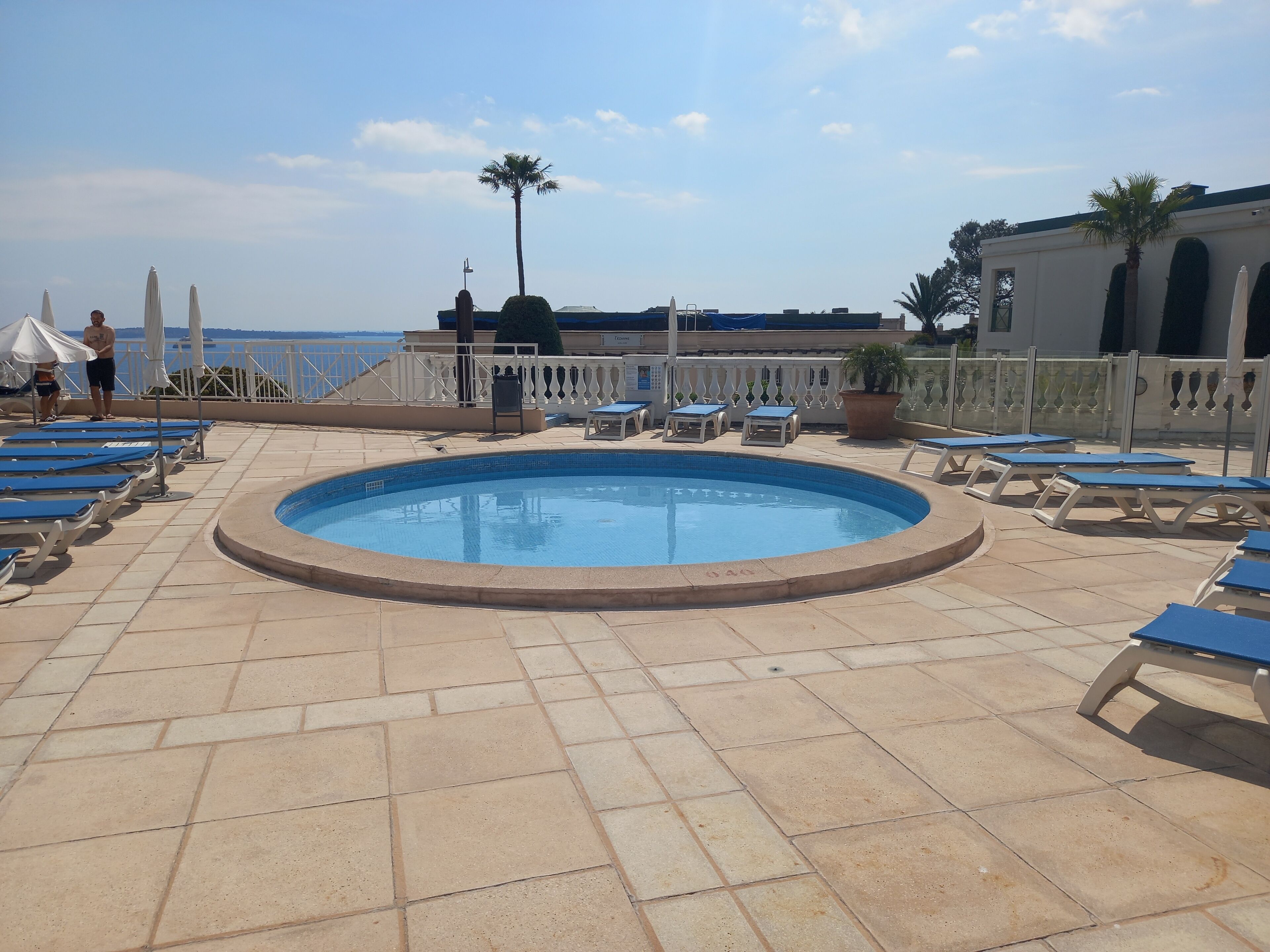 A pool area with blue lounge chairs, a small pool, and a view of the sea.
