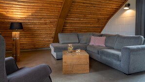 A cozy room with a sloped ceiling, a grey sectional sofa, a wooden coffee table, and a floor lamp. - Apartment in Netherlands with Scenic Meadows (Heeten)