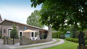 Un bâtiment doté d’une façade en pierre, d’un espace extérieur couvert aménagé en coin salon et d’une statue en premier plan.
