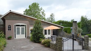 Une maison en briques avec une cheminée en pierre, une entrée fermée par un portail et une allée pavée.