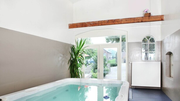 Une salle de spa dotée d’un jacuzzi, de poutres en bois, d’une grande plante en pot et offrant une vue sur le jardin extérieur.