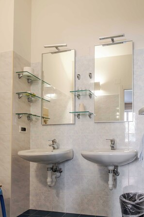 Un baño con dos lavamanos, estantes de vidrio y espejos.