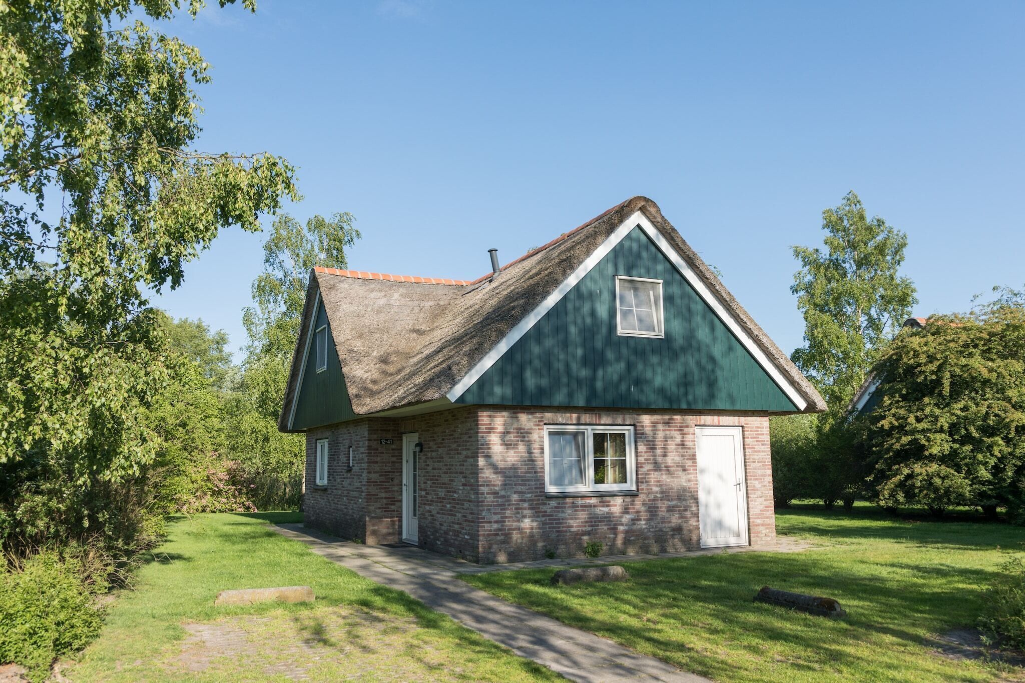 A single-story house with a green roof and brick walls, surrounded by trees and a grassy yard.