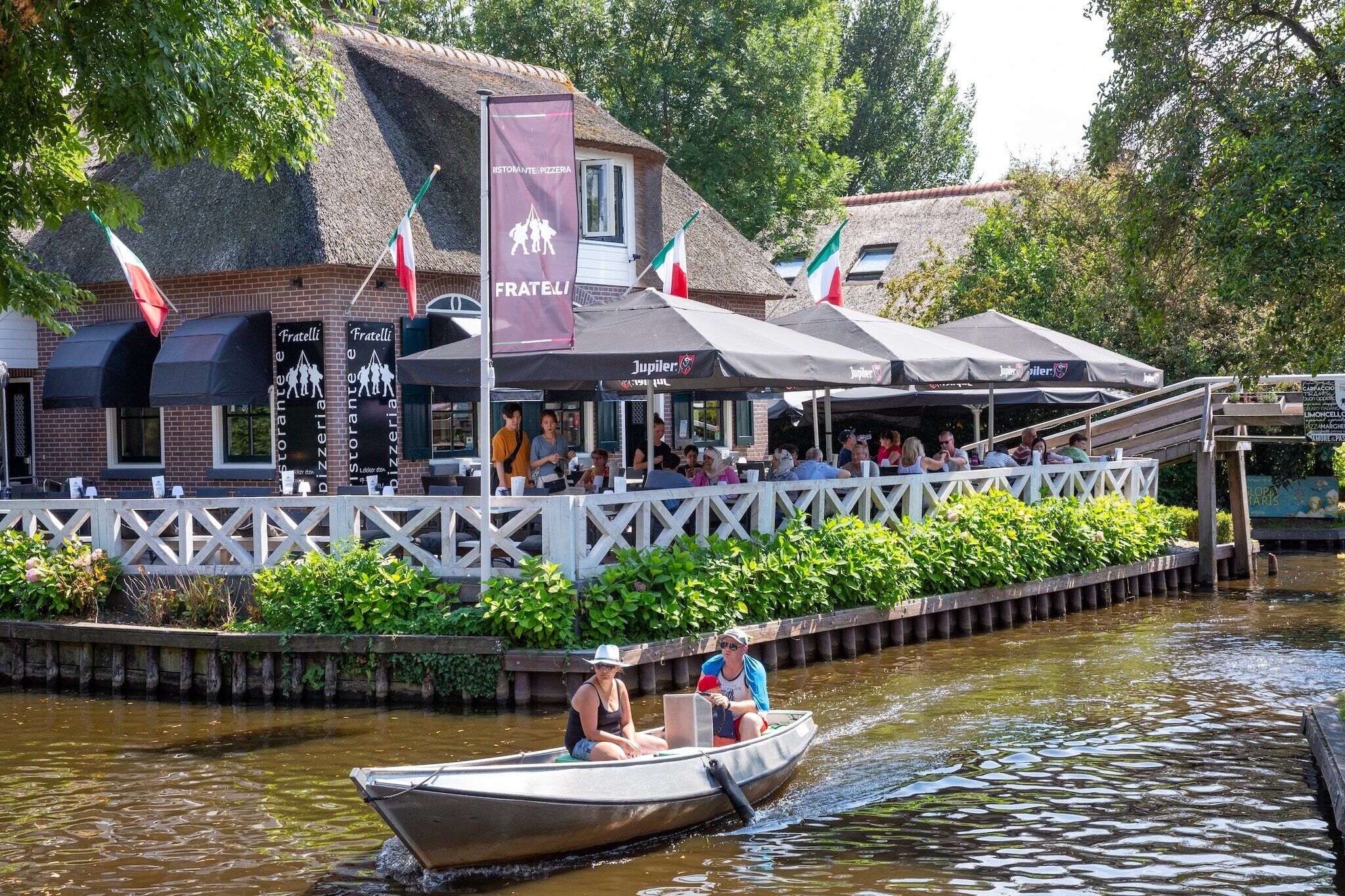 Un restaurant situé au bord de la rivière, avec une terrasse et un bateau qui passe.
