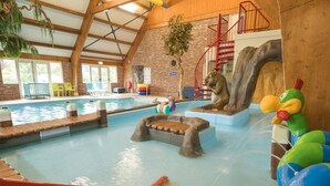 Una piscina interior amb tobogans i una zona de jocs per a infants, envoltada d'bigues de fusta i parets de rajola.