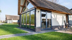 A modern house with a large glass extension, a thatched roof, and a well-maintained lawn. - Classy Holiday Home in Alphen with Garden (Alphen)