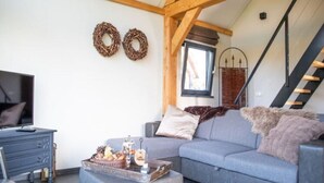 A cozy living room with a blue sofa, a small coffee table with snacks, a TV, and a staircase with a wooden railing. - Classy Holiday Home in Alphen with Garden (Alphen)