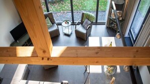 A modern interior with a high ceiling, a dining area with a table and chairs, and a view of the outdoors through large windows.