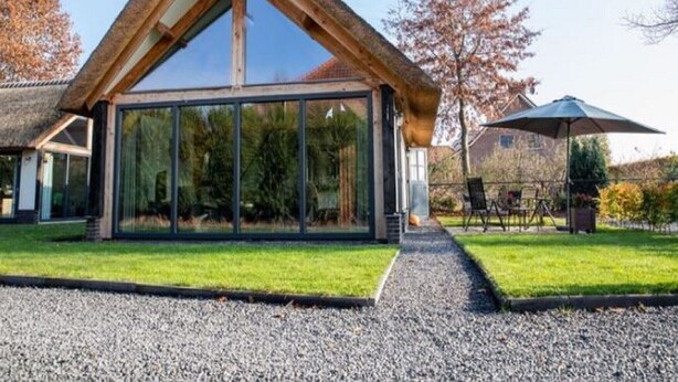 A modern house with a large glass facade, a sloped roof, and a gravel driveway.