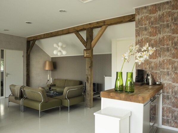 A modern living room with a sofa, chairs, a coffee table, and a kitchen area with a brick wall and green vases.