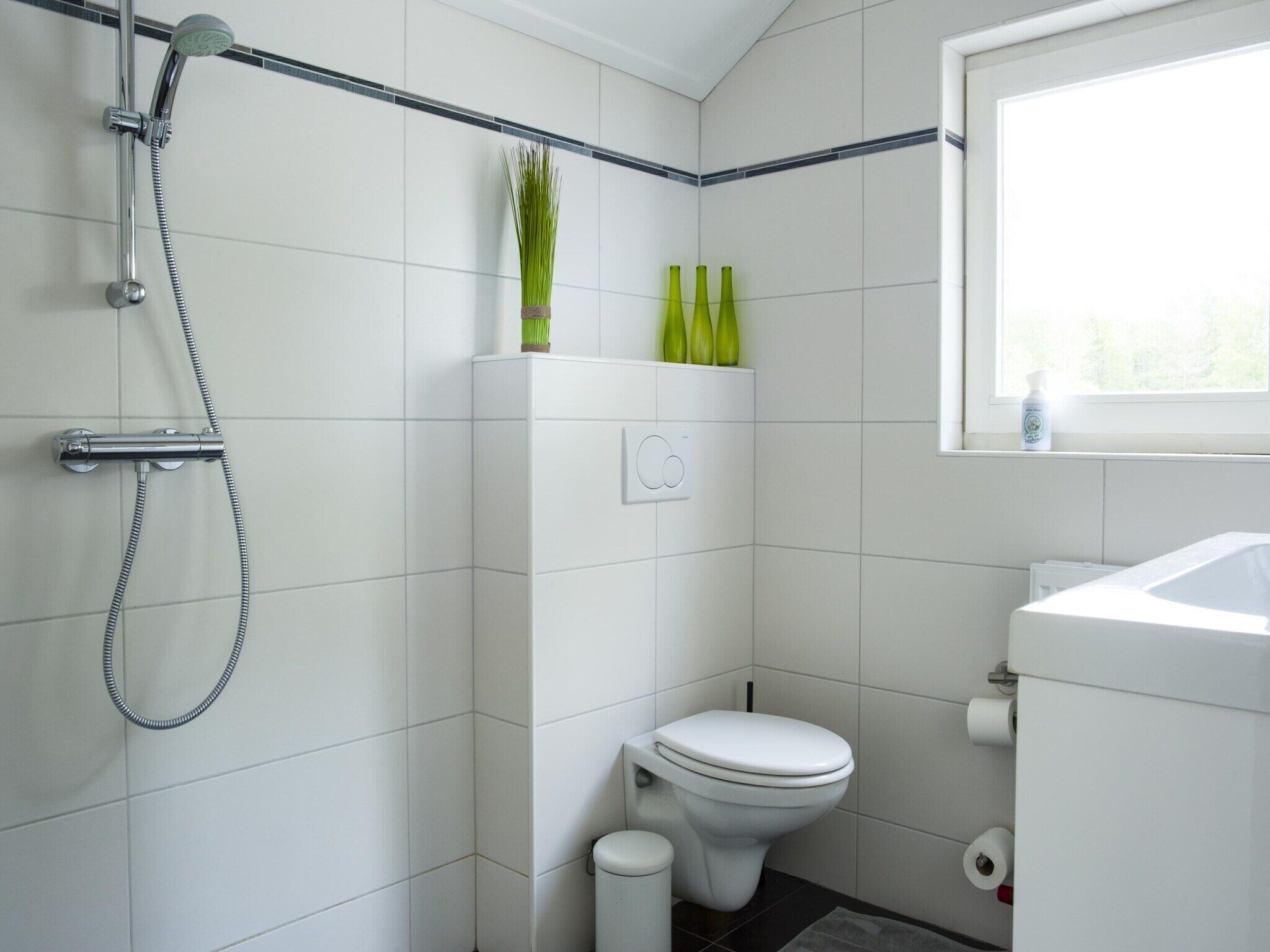 A modern bathroom with white tiles, a shower, a toilet, and a window.