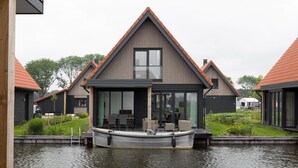 Une maison avec une jetée qui s’avance sur un plan d’eau, entourée de verdure et d’autres maisons similaires.