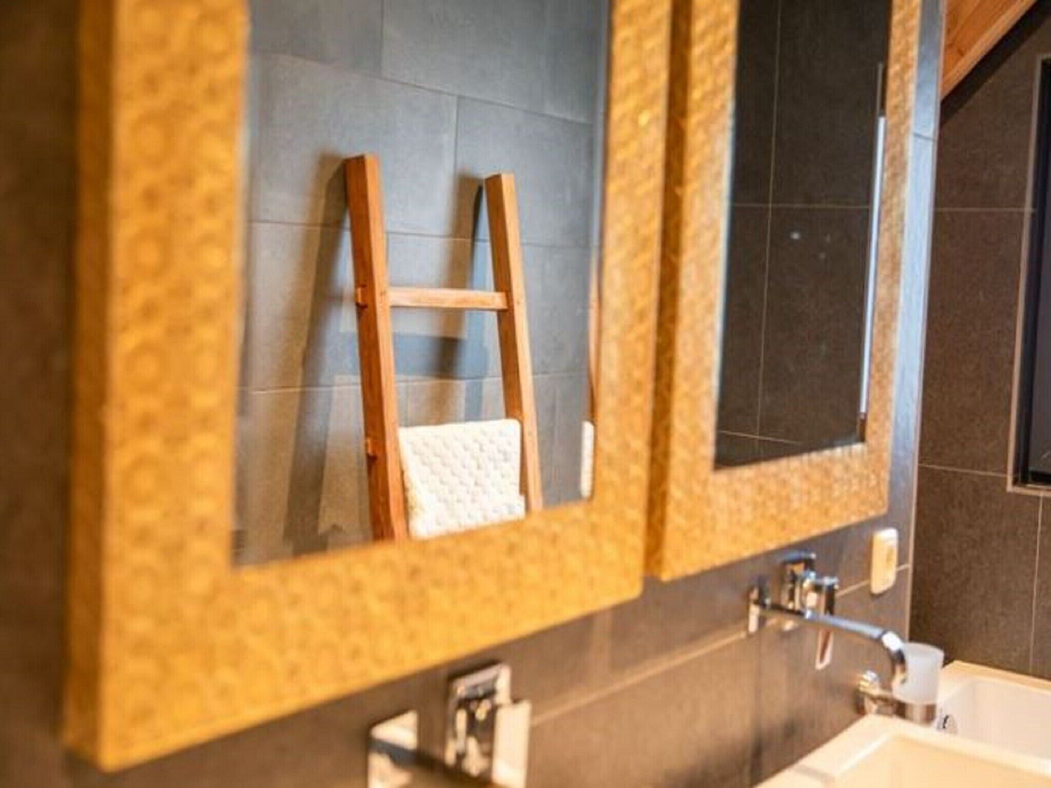 A bathroom with a large mirror, a wooden ladder leaning against the wall, and a white towel hanging on the mirror.
