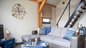 Un salon moderne avec un canapé d’angle gris, une table d’appoint bleue et une horloge au mur.