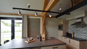 Een moderne keuken met een groot eiland, houten kastjes en een zwart aanrecht. Boven het eiland hangen twee hanglampen, en er is een prikbord waarop 'Villa Bianco' staat.
