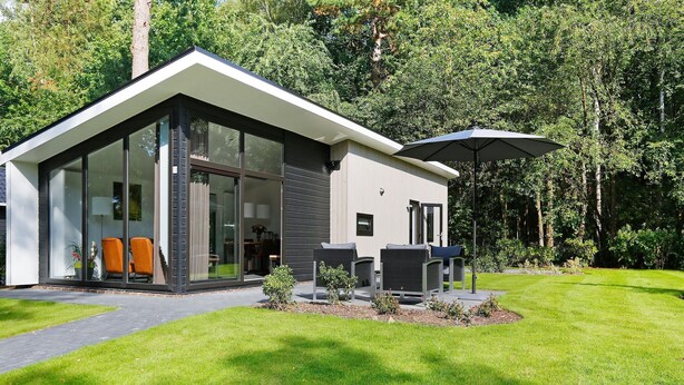 Een modern huis met een glazen entree, terras buiten en een verzorgd gazon.