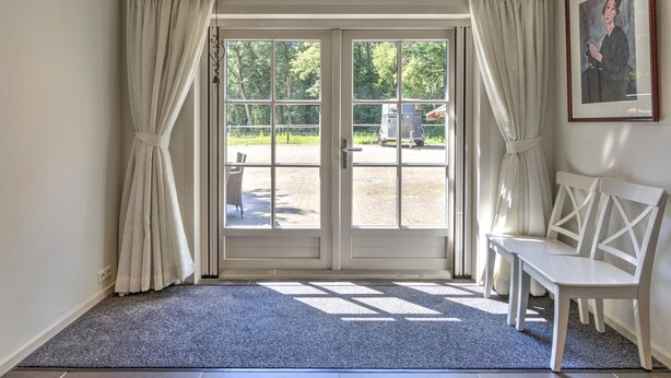 Ein Zimmer mit einer großen Glastür, die nach draußen führt, einer weißen Bank und einem gerahmten Bild an der Wand.