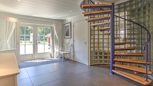 Ein geräumiges Zimmer mit einer geschwungenen Holztreppe und einem großen Fenster mit Blick ins Freie.
