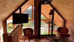 Una habitación acogedora con un gran ventanal, televisor, dos sillas y una mesita.