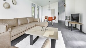 A modern living room with a beige sectional sofa, a wooden coffee table, and a dining area with orange chairs. - Chalet in Zell am See near Ski Slope (Markelo)