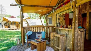 Una terrassa de fusta amb un sofà i una taula, envoltada d'intents i una zona de bar.