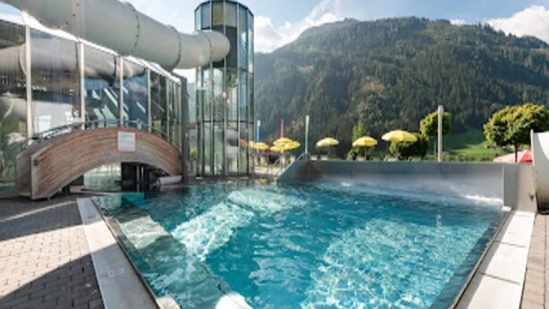 Una piscina con un puente de cristal y montañas al fondo.