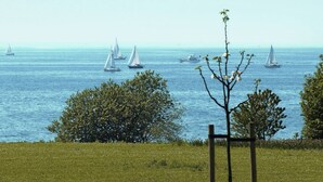 Vista costera con veleros en el agua, un primer plano con hierba y un poste de madera.
