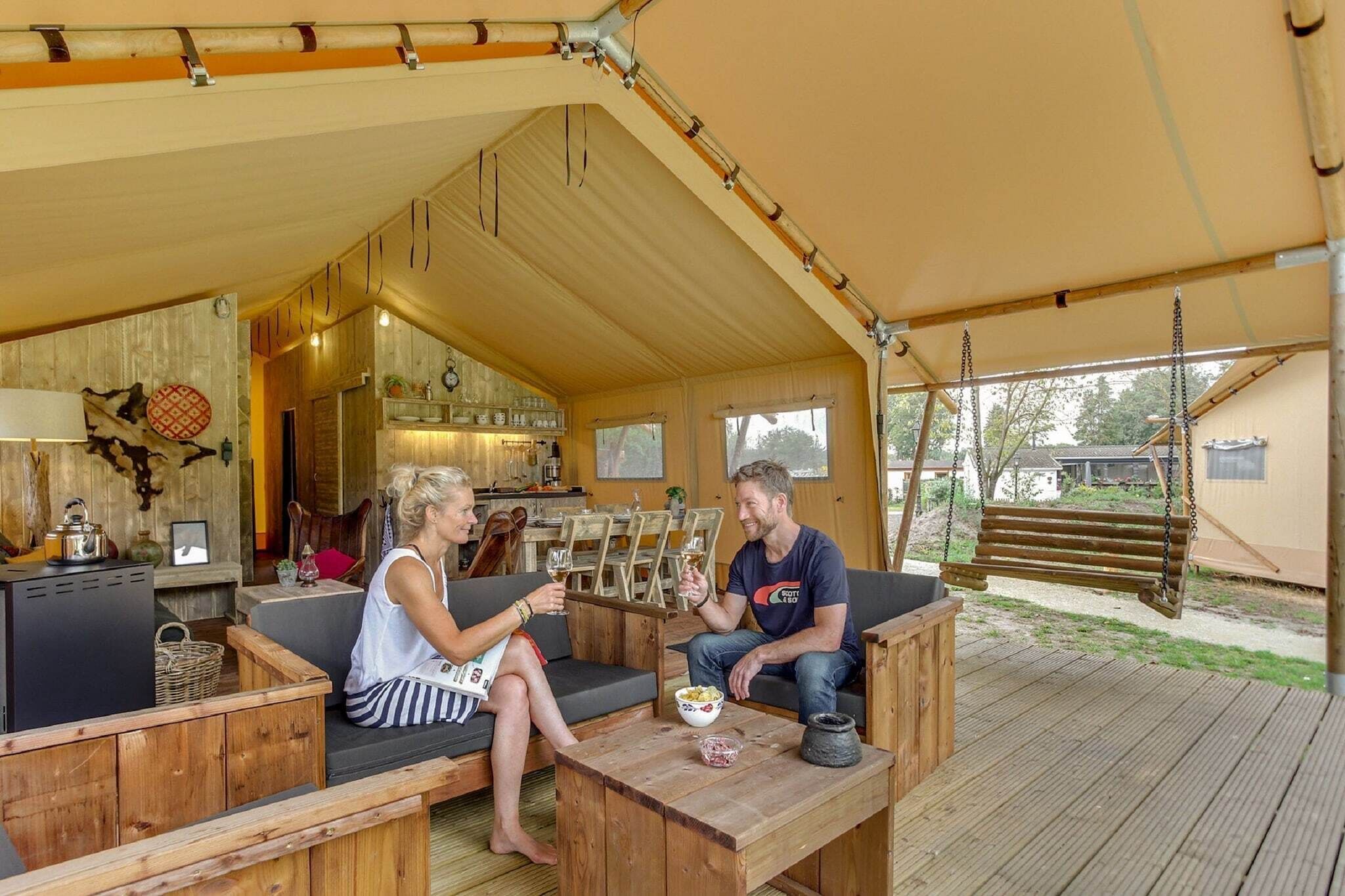 A wooden deck with a covered seating area, a kitchen in the background, and a hanging swing.