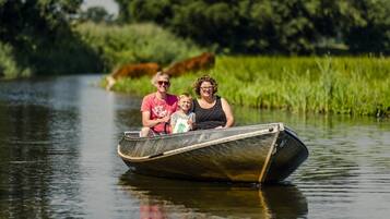 Uma família num barco estreito num rio calmo, rodeada por vegetação.