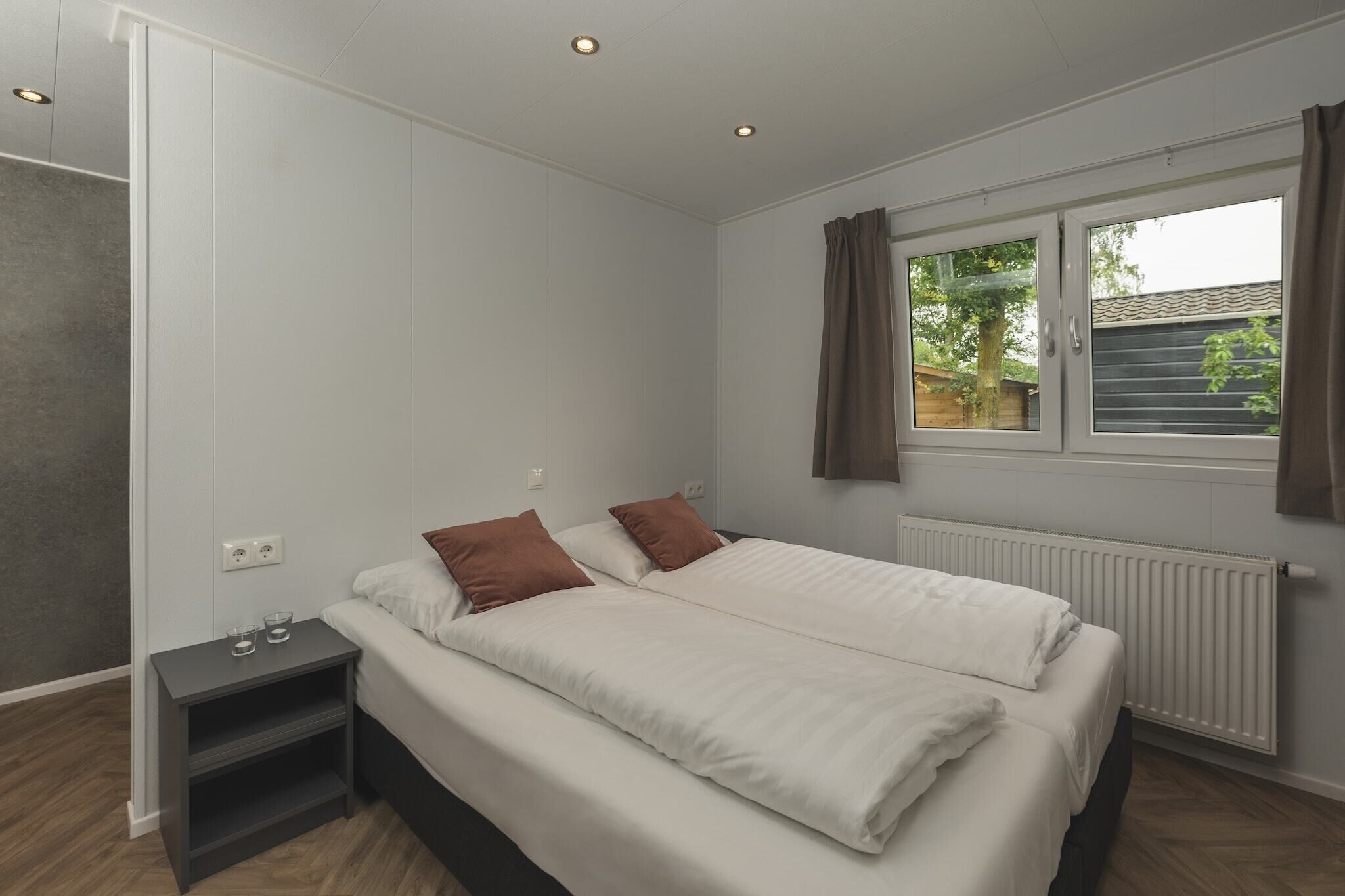 Een slaapkamer met een bed, nachtkastje, raam met gordijnen en een radiator.