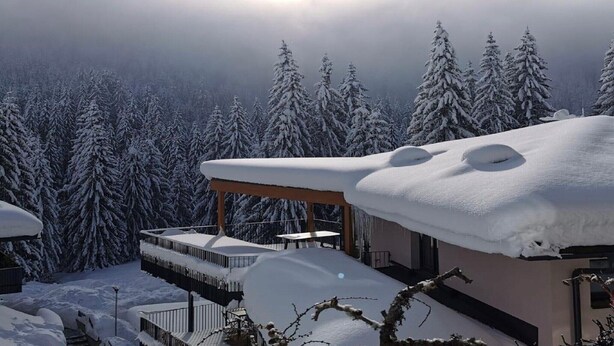 A snow-covered landscape with a building featuring a balcony and a covered outdoor area.