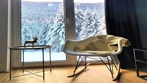 A room with a large window offering a view of a snowy forest.