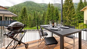 An outdoor dining area with a table set for two, a grill, and a scenic mountain view.