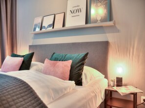 Una cama bien hecha con varias almohadas, una mesita de noche con lámpara y citas inspiradoras enmarcadas en la pared.