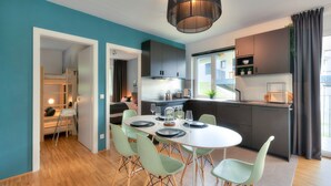 A modern kitchen with dark cabinets, a round dining table with green chairs, and a hanging light fixture.