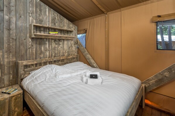 A wooden bed with white bedding, a wooden nightstand, and a shelf with books.
