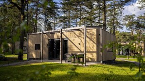 Una cabaña de madera con puerta, ventanas y un pequeño espacio de estar al aire libre.