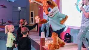 Une personne déguisée en lapin, sur une scène, tenant un micro. Un écran de projection affiche les mots « Room » et « Welcome ». Un enfant interagit avec la personne.