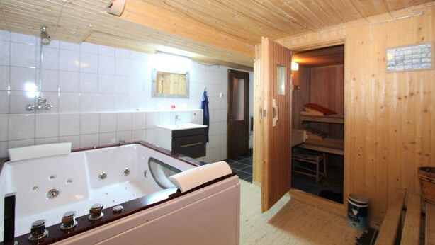 Ein Holzinnenraum mit einer Badewanne, einem Waschbecken und einer Saunatür.
