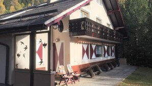 Ein Chalet mit Balkon, einer hölzernen Bank und Blick auf den Wald.