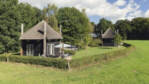 Deux charmantes chaumières aux toits de chaume et aux façades en bois, entourées d’une végétation luxuriante et d’arbres.