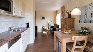 Une cuisine moderne avec des meubles blancs, un plan de travail en bois et un coin repas comprenant une table et des chaises en bois.
