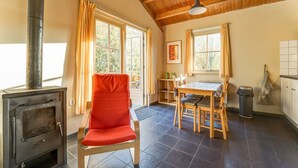 A cozy room with a wood-burning stove, a dining table with chairs, and a window with curtains. - Holiday home with terrace (Lage Zwaluwe)