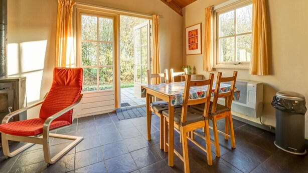 A cozy dining area with a table and chairs, a red chair, a heater, and a window with curtains. - Holiday home with terrace (Lage Zwaluwe)