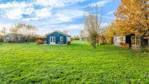 A blue house with a front porch, surrounded by a grassy field and trees with autumn leaves. - Holiday home with terrace (Lage Zwaluwe)